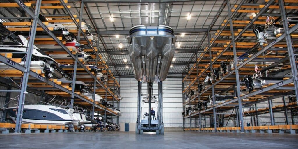 Aerial-style interior view of a dry stack marina storage facility with boats stored on racking systems and a marine forklift used for vessel handling.